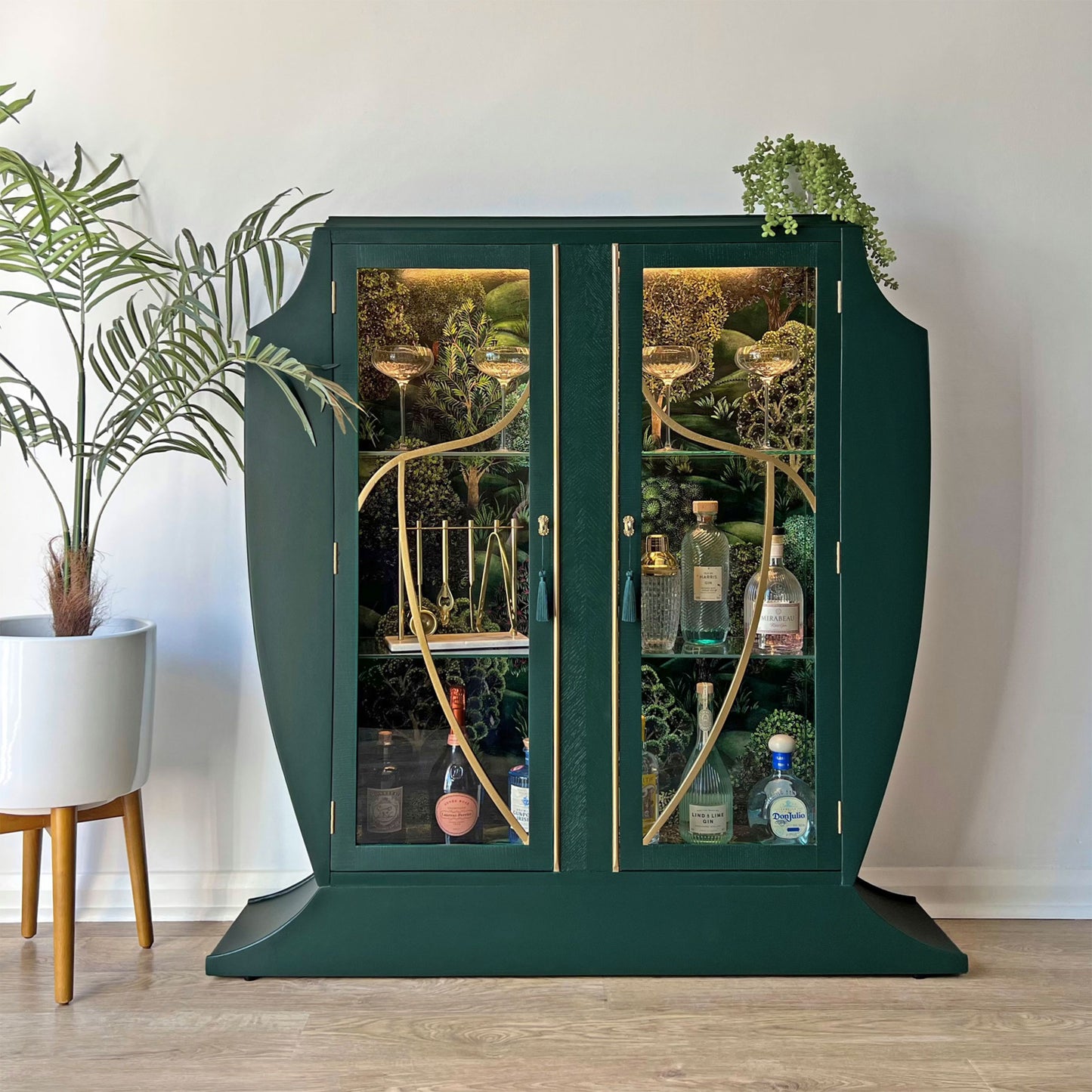 Luxurious green Art Deco cocktail cabinet styled with spirits and glassware, featuring gold accents and Cole & Son Forest interior.