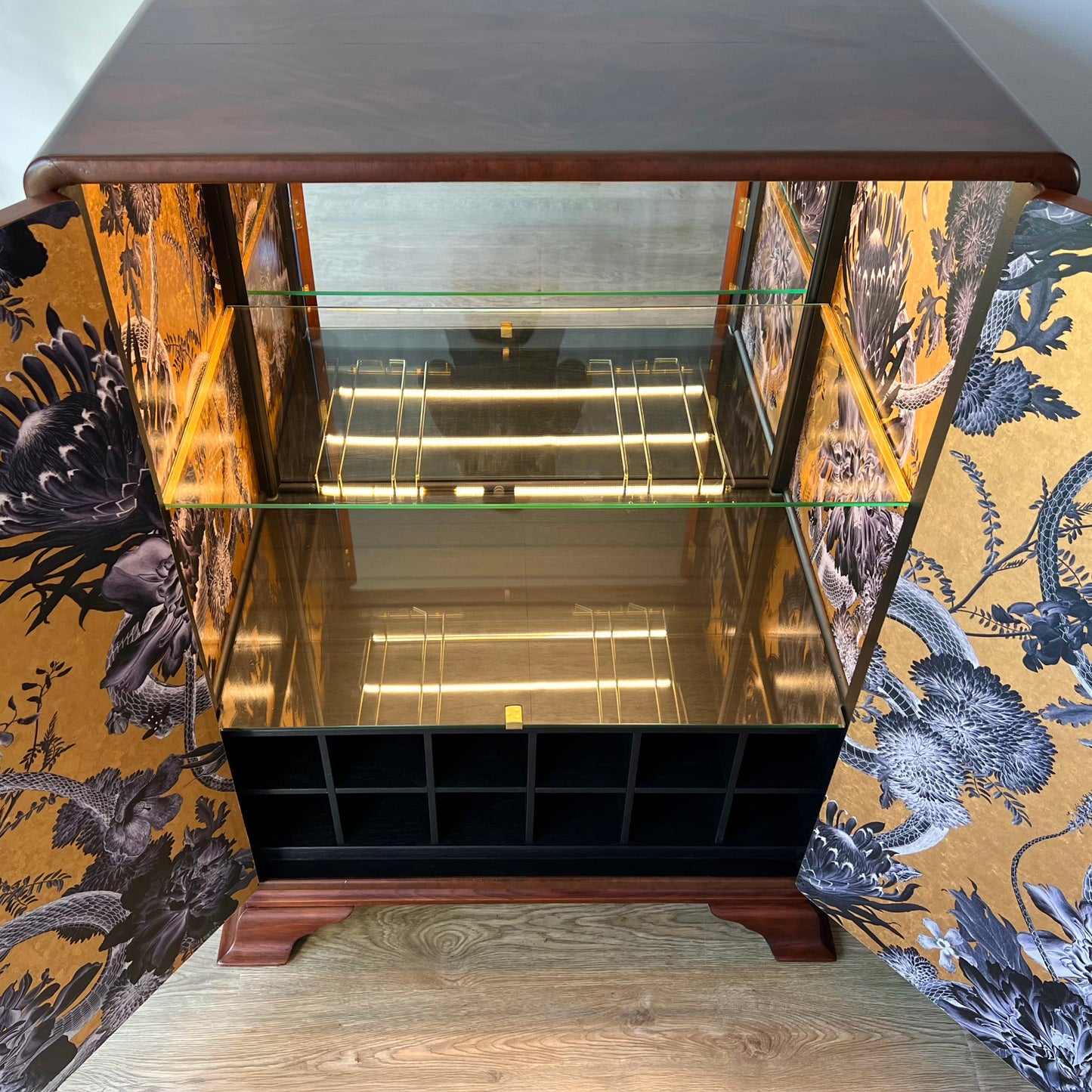 Bird's-eye view of the illuminated interior with glass shelves, glass base, and golden-hued wallpaper in a high-end Art Deco cocktail cabinet.