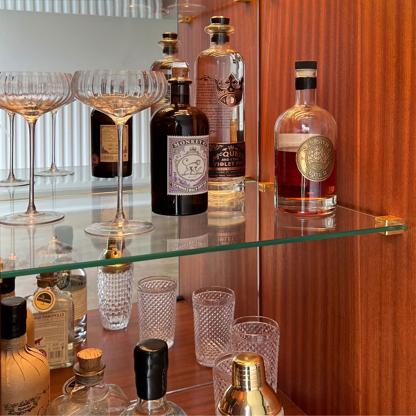 Motion-activated LED lighting illuminating the glass shelves of a bespoke G Plan Librenza drinks cabinet, highlighting spirits and glassware.