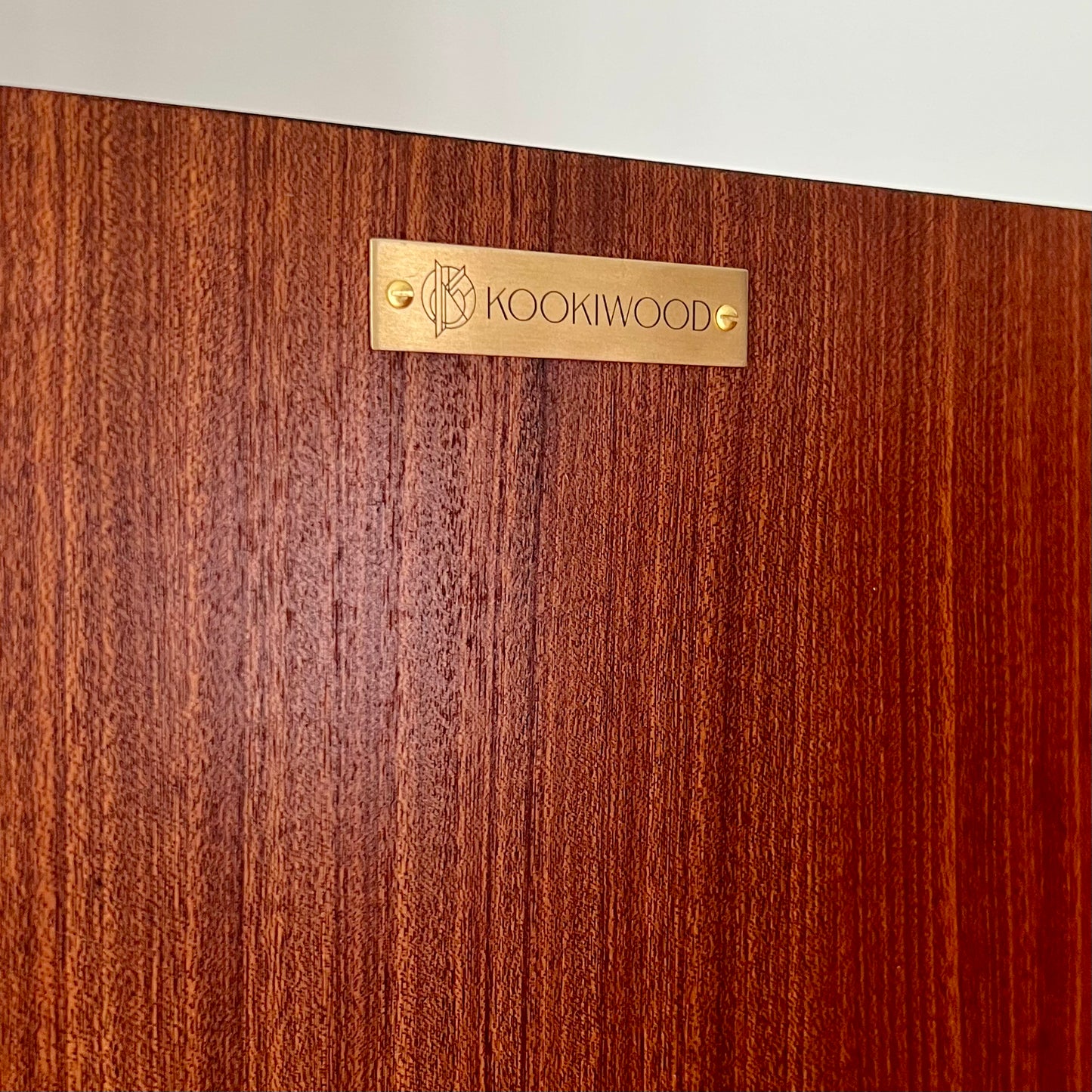 Close-up of Kookiwood brass branding tag affixed to the G Plan Librenza drinks cabinet, signifying bespoke craftsmanship and luxury design.