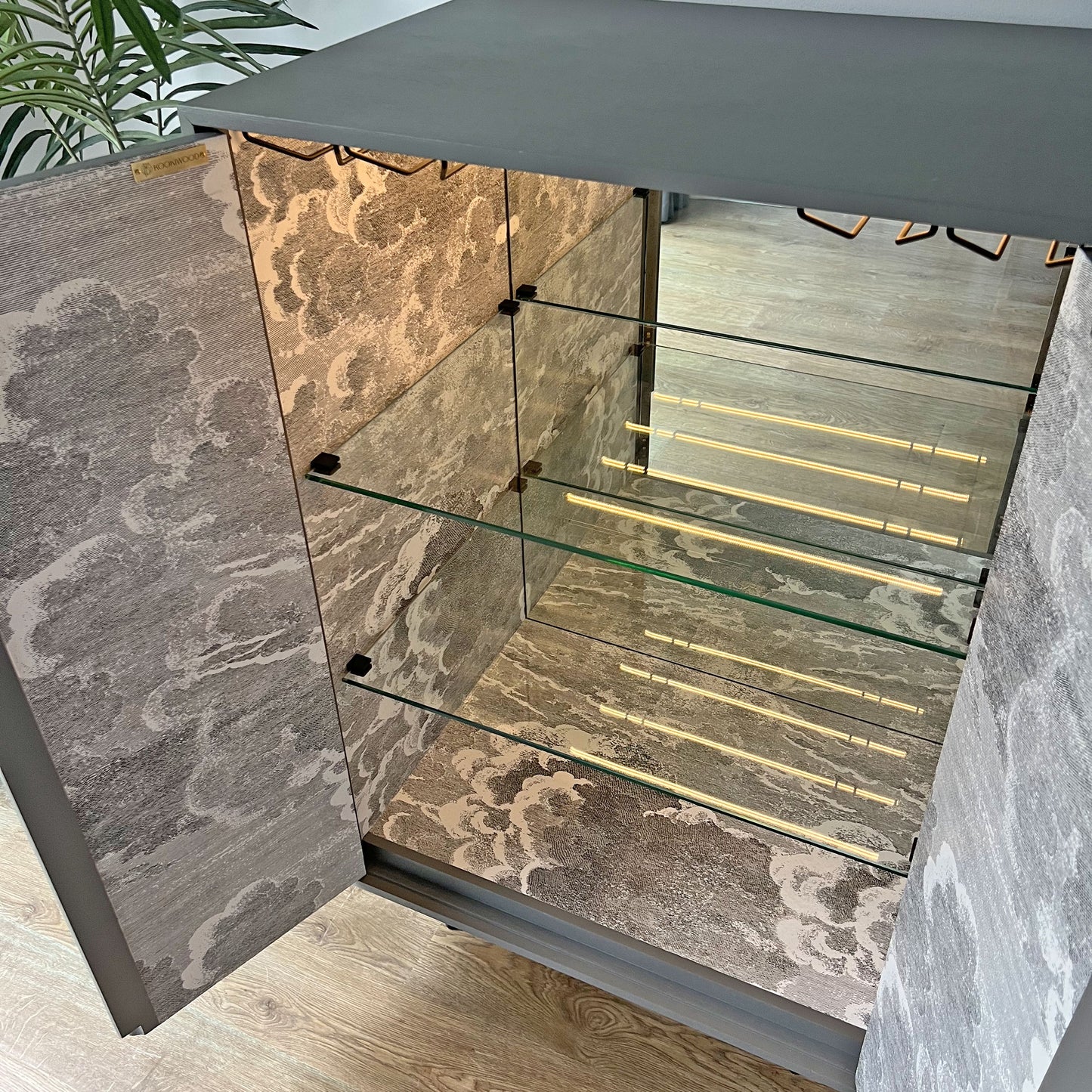 Luxury drinks cabinet interior with thick glass shelves and four integrated brass glass racks for stylish stemware storage.