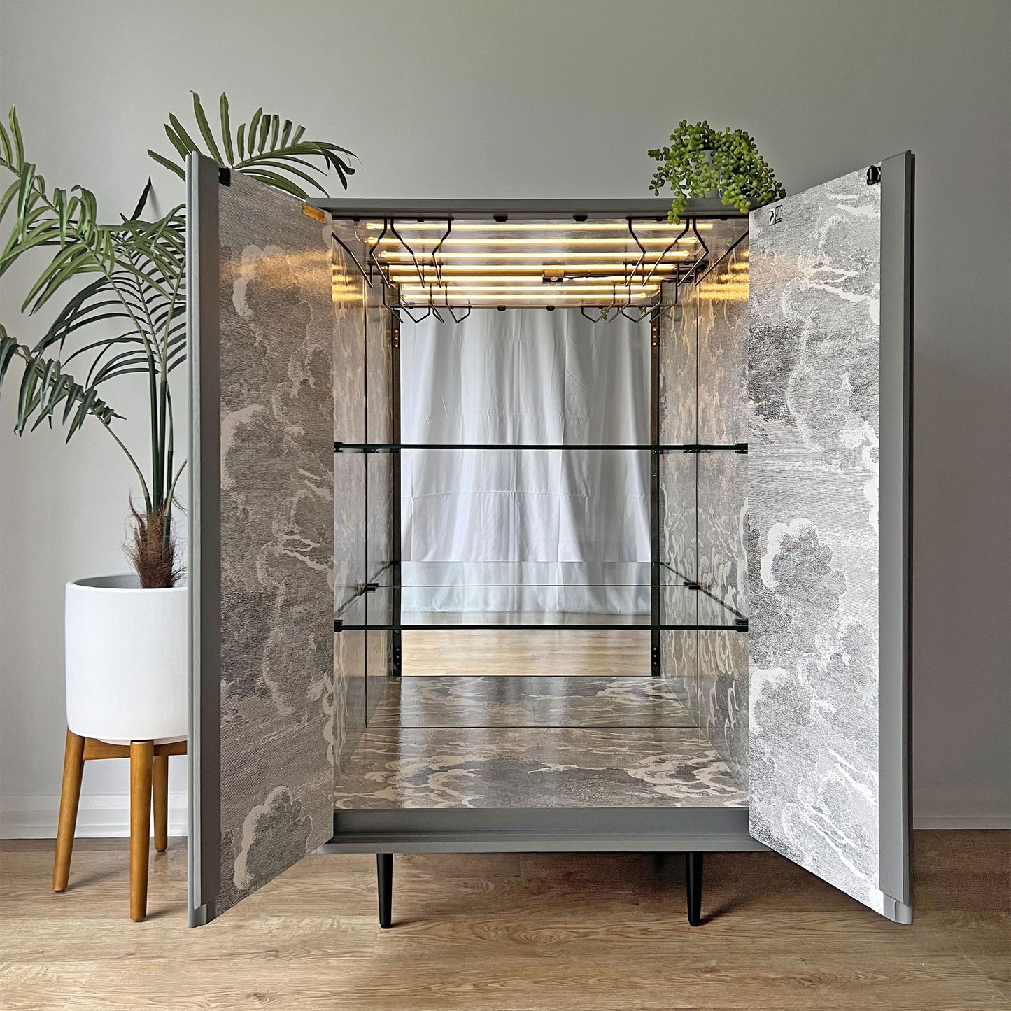 Luxury cocktail cabinet interior featuring Fornasetti 'Nuvolette' cloudscape wallpaper, glass shelves, and motion sensor LED lighting.