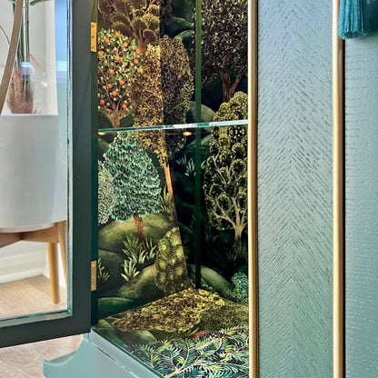 Close-up of premium Cole & Son Forest wallpaper used inside green vintage drinks cabinet with fixed glass shelving.