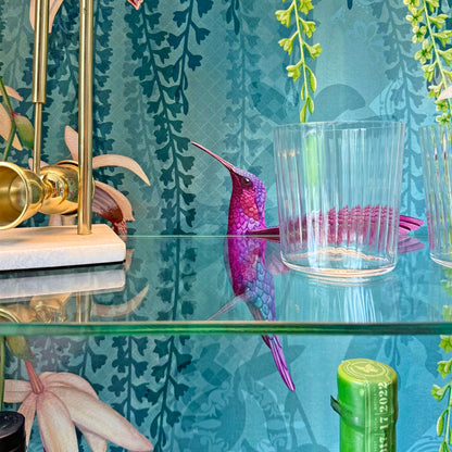 Detailed view of Osborne & Little ‘Trailing Orchids’ wallpaper inside a teal cabinet, featuring a pink hummingbird and glass shelf.