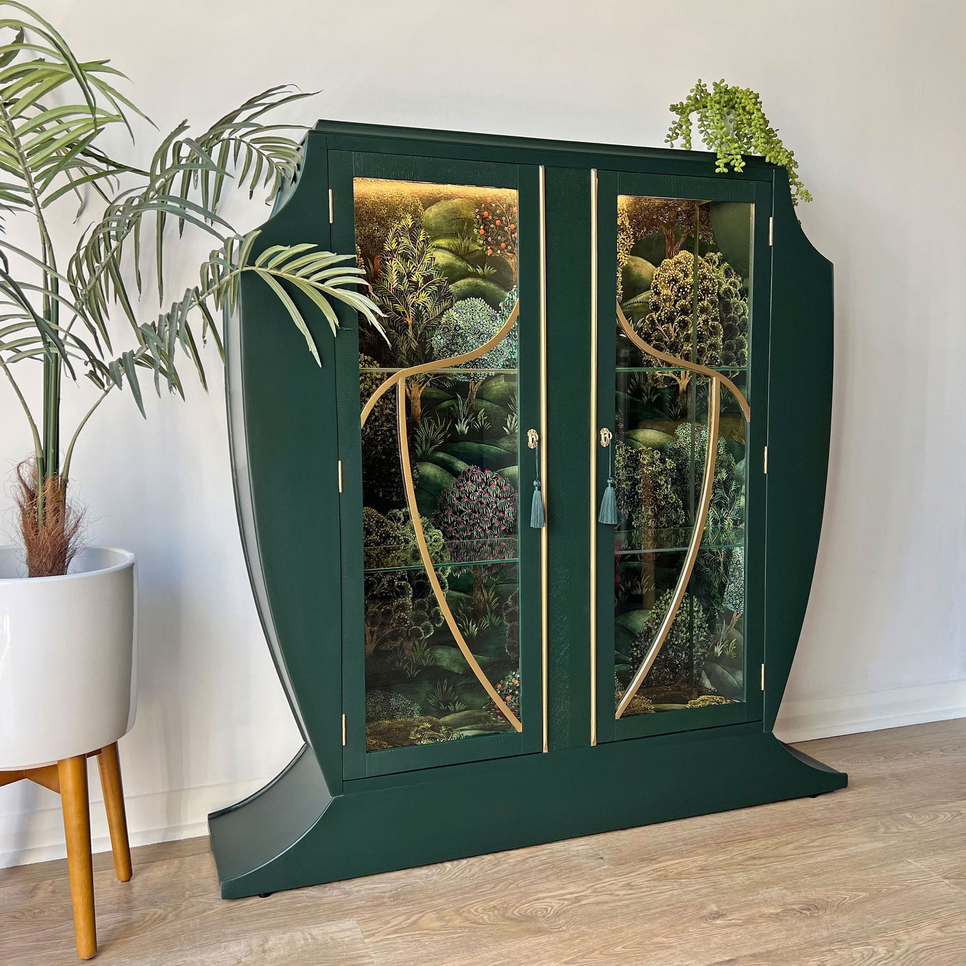 Full view of green Art Deco cocktail cabinet with  gold detailing, and Cole & Son Forest backdrop.