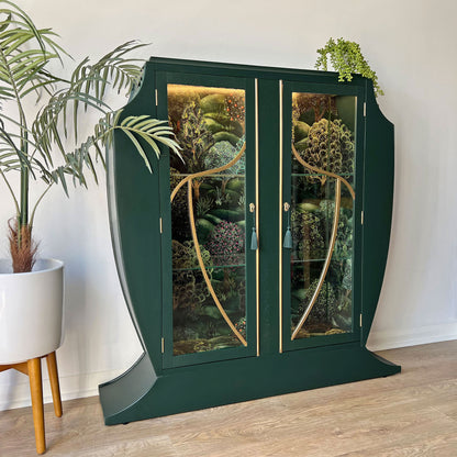Full view of green Art Deco cocktail cabinet with  gold detailing, and Cole & Son Forest backdrop.