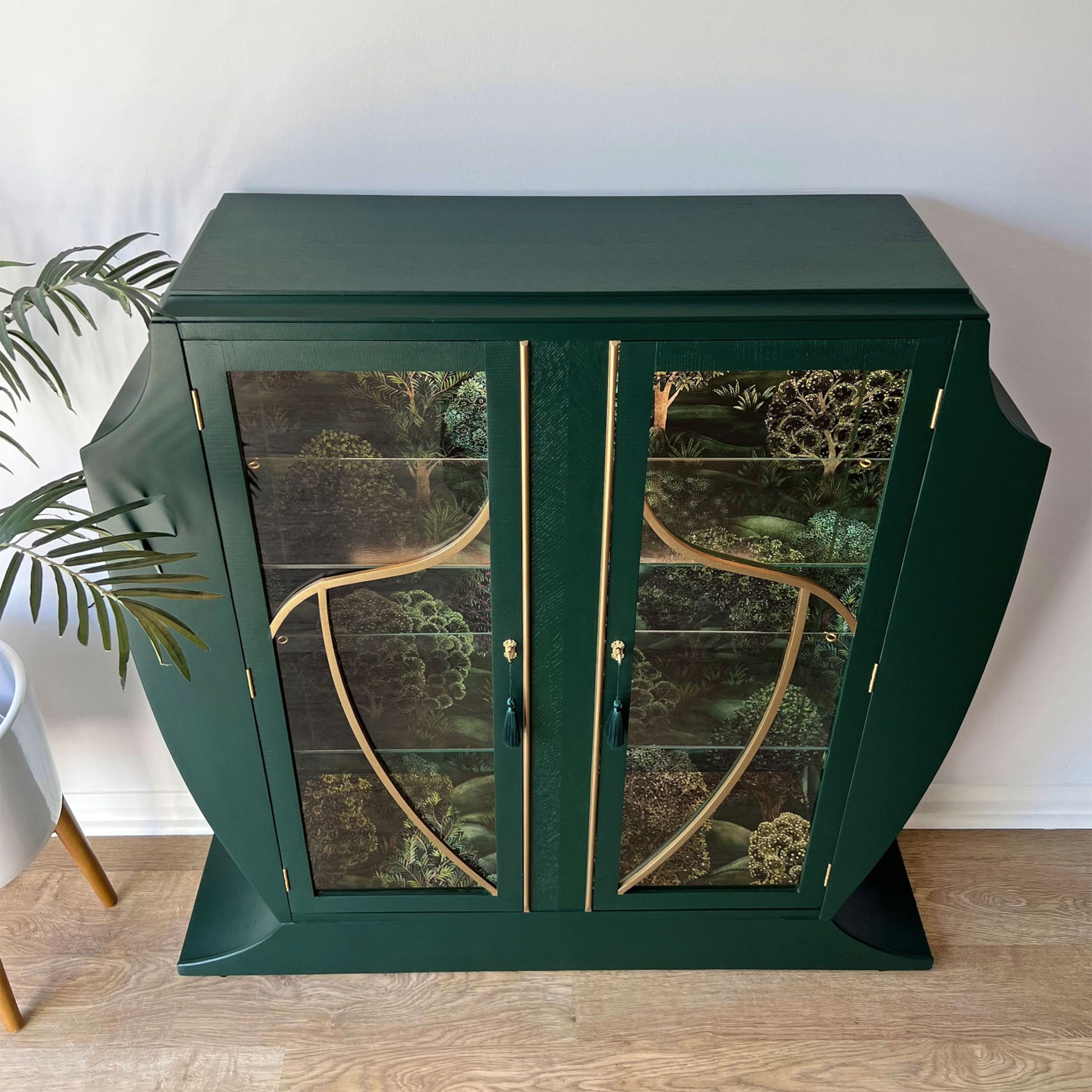 Overhead view of a green Art Deco drinks cabinet with Cole & Son "Forest" wallpaper interior and glass doors.