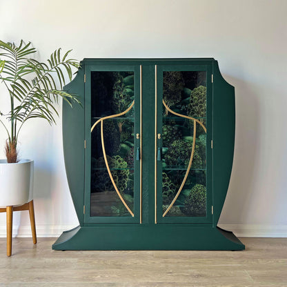 Front view of closed green Art Deco cocktail cabinet featuring glass doors and Cole & Son Forest design backing.