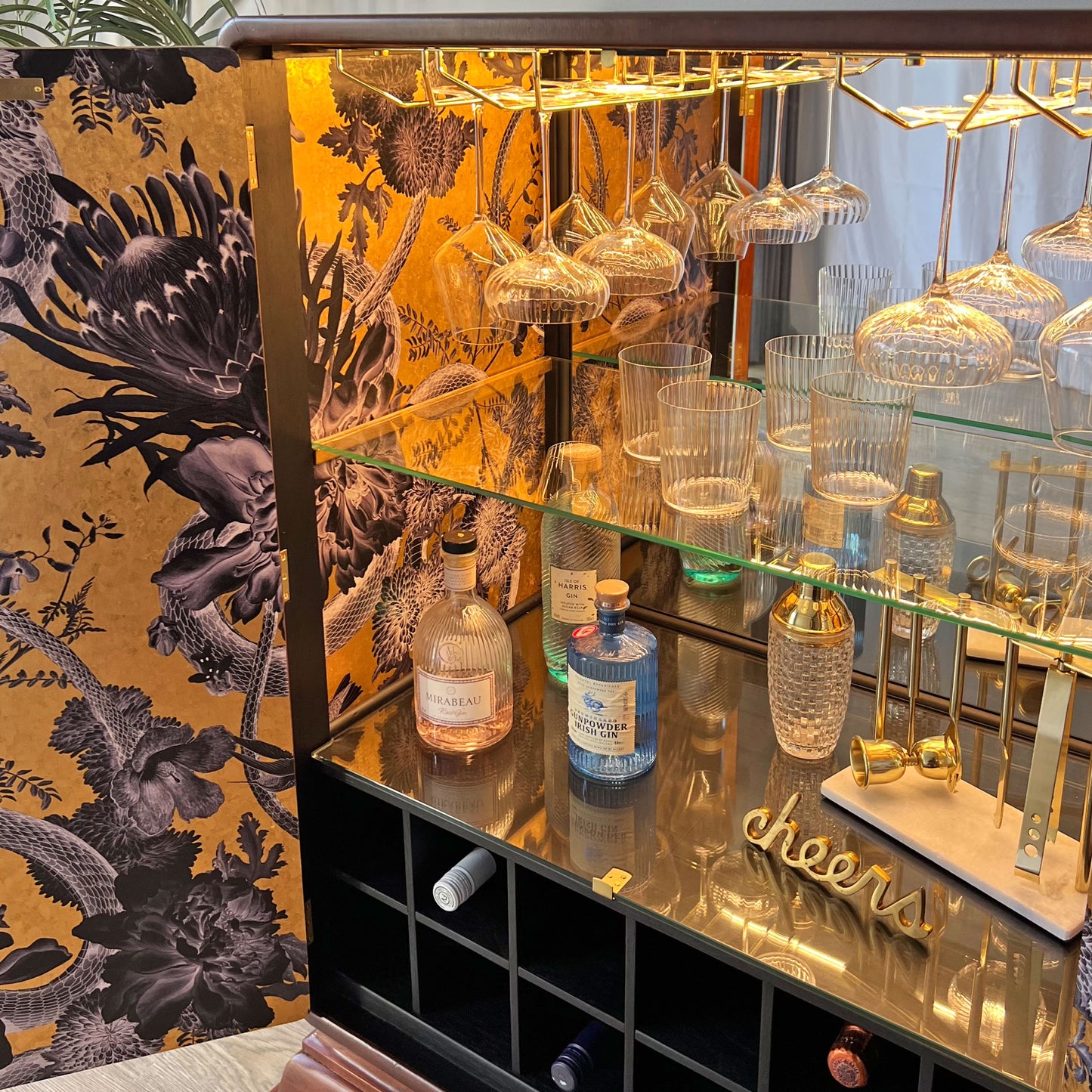 Hanging crystal glassware and premium spirits displayed under warm LED lighting inside a mirrored Art Deco bar cabinet.