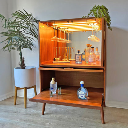 This mid-century G Plan cocktail cabinet is fully styled with glassware and spirits, featuring a mirrored back, LED lighting, and bespoke brass glass racks.
