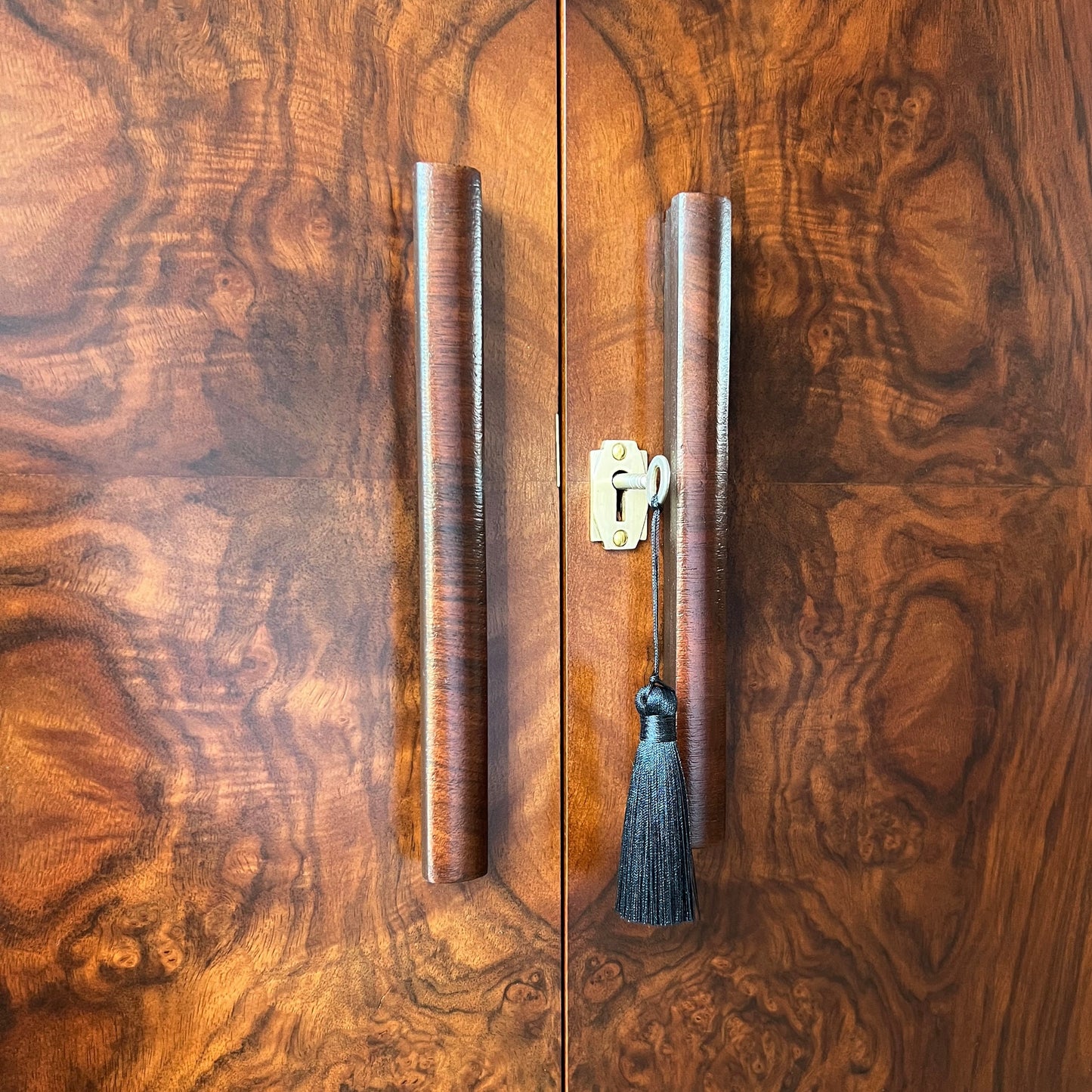 Detailed close-up of curved original walnut handles and brass lock with tassel on the doors of an Art Deco drinks cabinet.