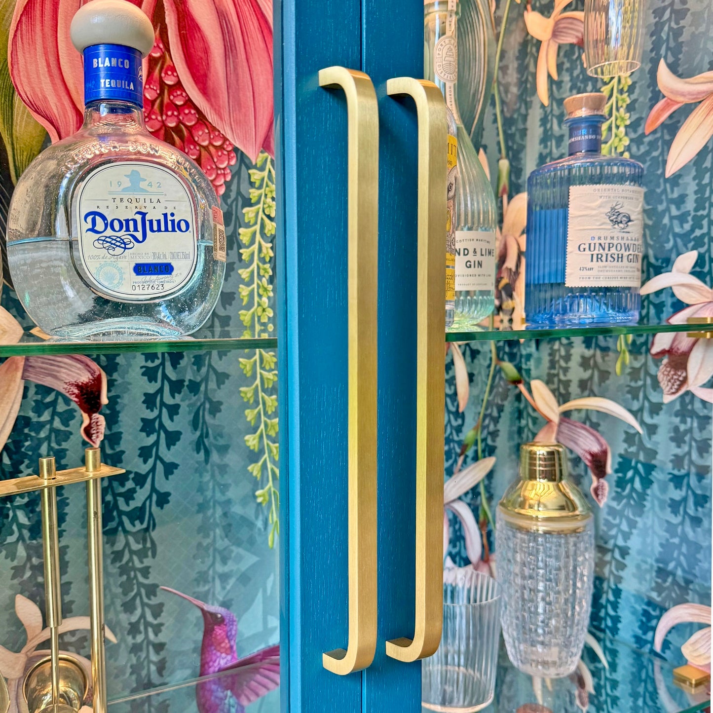 Close-up view of elegant curved brass handles and floral wallpaper inside a luxury display cabinet.