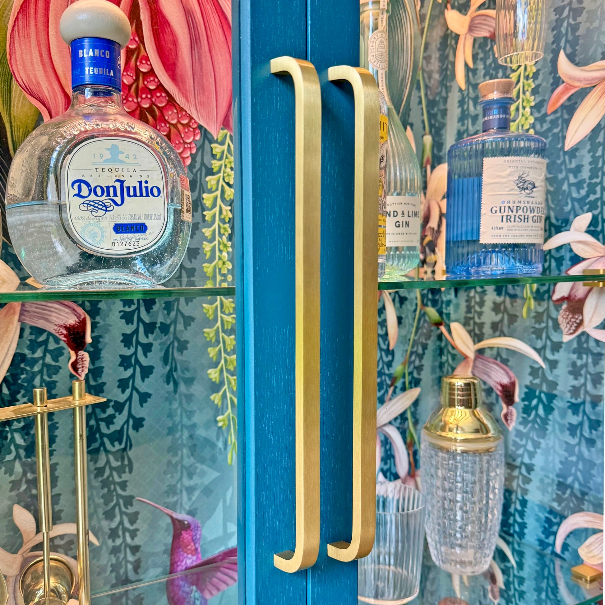 Close-up view of elegant curved brass handles and floral wallpaper inside a luxury display cabinet.
