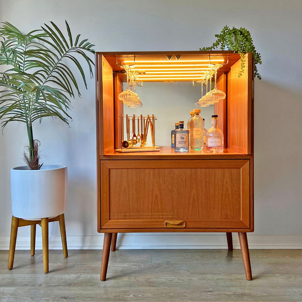 This vintage G Plan cocktail cabinet is fully styled with glassware and spirits, featuring a mirrored back, LED lighting, and bespoke brass glass racks.