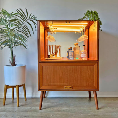 This vintage G Plan cocktail cabinet is fully styled with glassware and spirits, featuring a mirrored back, LED lighting, and bespoke brass glass racks.