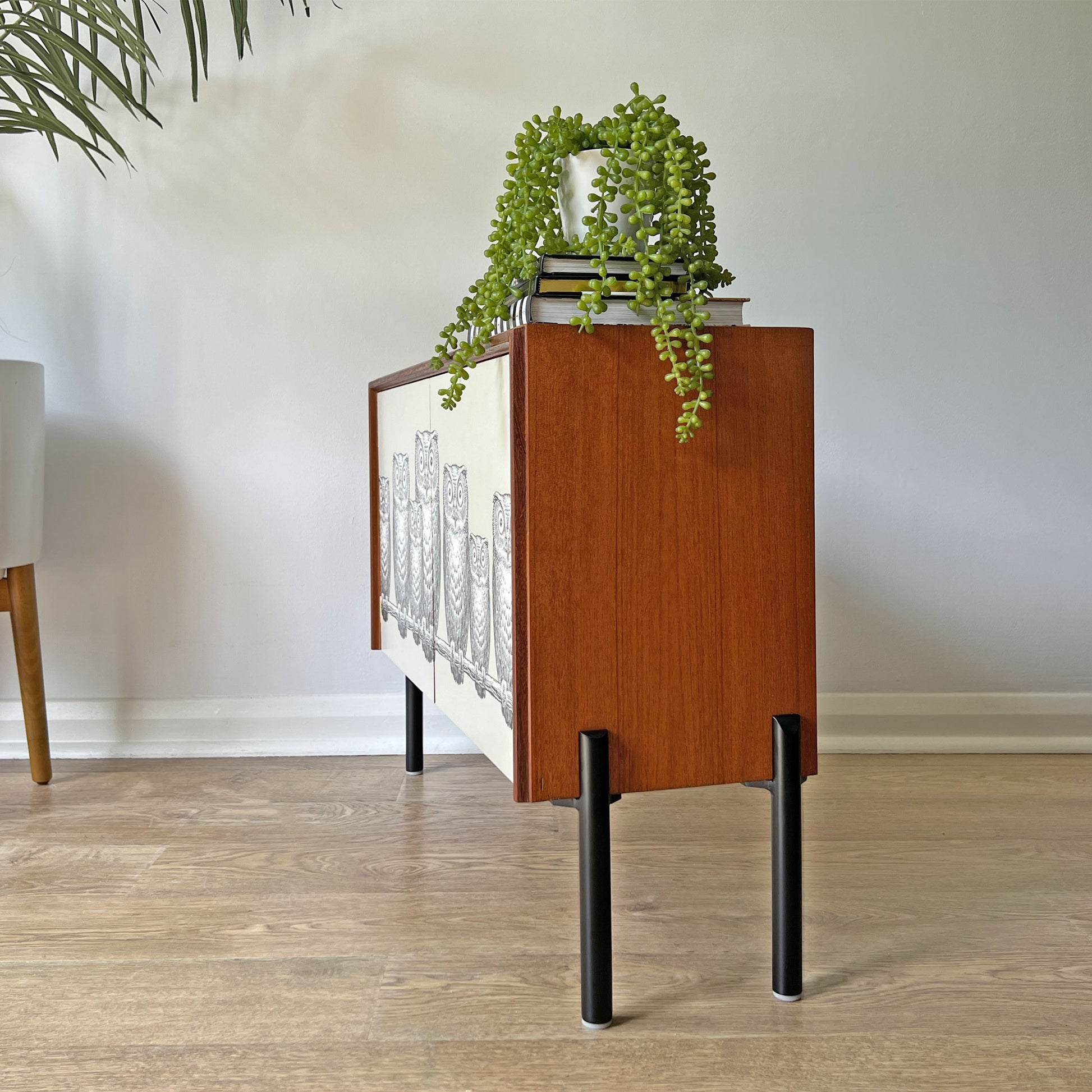 Sleek matte black legs on G Plan cabinet, offering a contemporary contrast to the whimsical Fornasetti ‘Nottambule’ owl print.