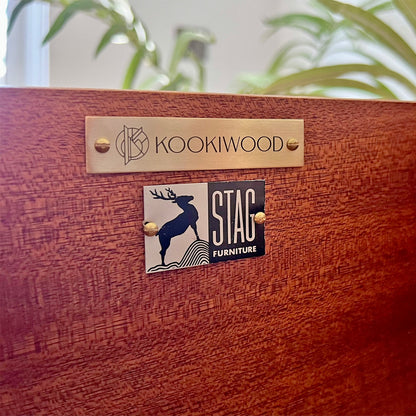 Close-up of Kookiwood brass branding tag affixed to the Stag C Range tallboy, signifying bespoke craftsmanship and exclusivity.