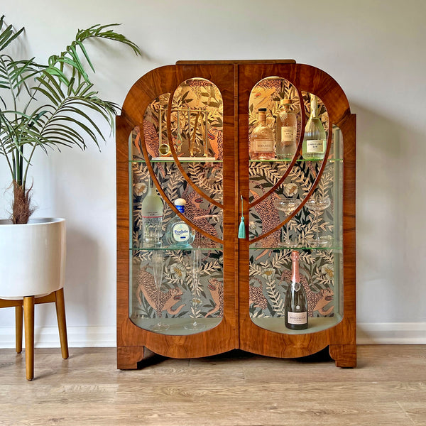 Vintage walnut drinks cabinet styled in a luxury home setting, serving as an elegant bar area with glassware and wine bottles.